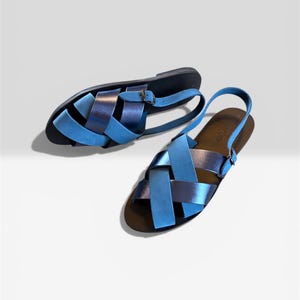May include: A pair of blue leather sandals with a woven design. The sandals have light and dark blue straps, a black sole, and a buckle fastening. These sandals are designed for comfort and style, perfect for warm weather.