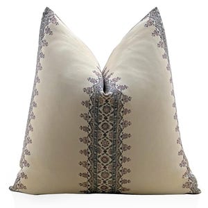 May include: Cream-colored decorative pillow with a detailed floral pattern in shades of gray and mauve. The pillow features a central vertical band of intricate designs, bordered by a repeating floral motif along the edges. The pillow is a square shape.