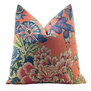 May include: A decorative cushion with a vibrant floral pattern. The cushion features large, stylized flowers in shades of pink, blue, and green against a coral background. The design includes detailed leaves and petals, creating a botanical theme.