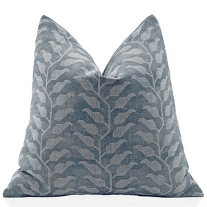 May include: A square decorative pillow with a blue-gray background and a repeating pattern of stylized, light gray leaves. The leaves are arranged in vertical, branch-like formations across the pillow's surface. The pillow has a soft, textured appearance.