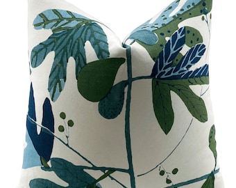 May include: A white pillow cover featuring a blue and green leaf design. The leaves are stylised and abstract, with some resembling fig leaves.