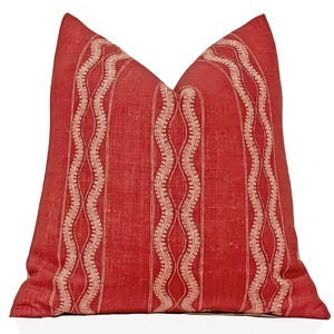 May include: A red decorative pillow with a textured appearance. The pillow features vertical stripes with a cream-colored, wavy embroidered design. The pillow is a square shape and is likely used for home decor.