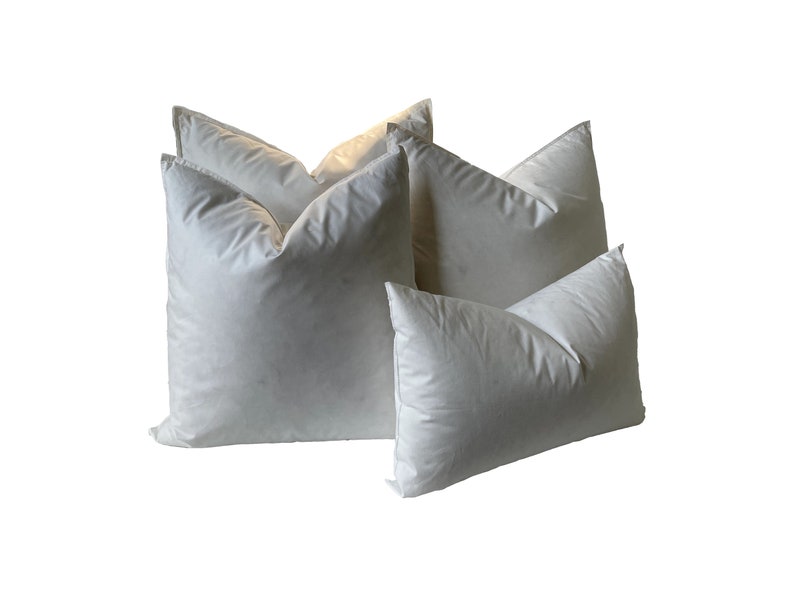 May include: Four white down-filled pillows of varying sizes. The pillows are arranged in a staggered formation, with the largest pillow at the back and the smallest pillow at the front.