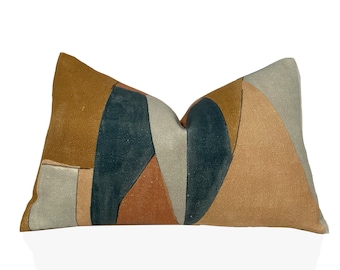 Puede incluir: Una almohada rectangular con un patrón geométrico en tonos marrones, beige, azul verdoso y gris.