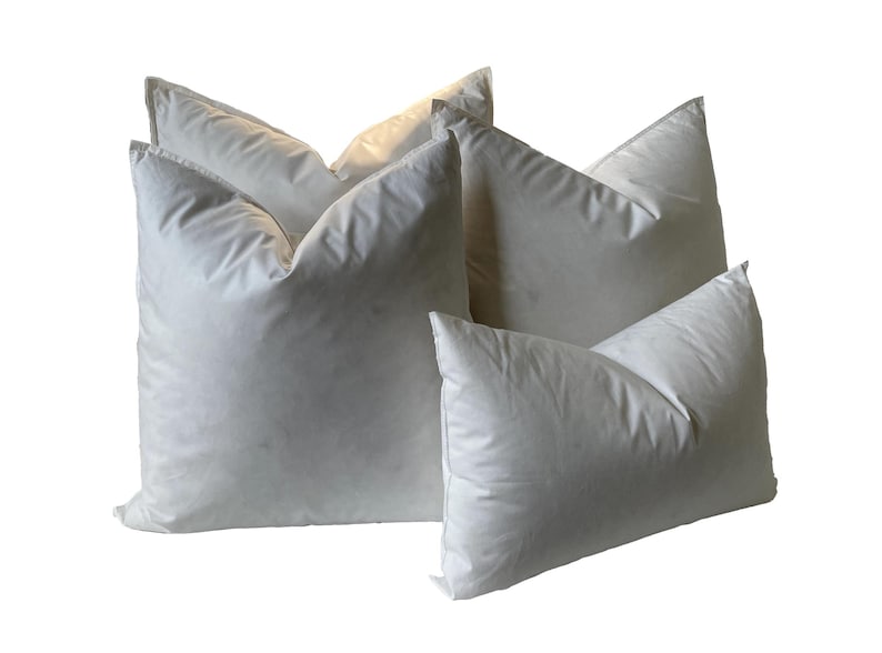 Puede incluir: Cuatro almohadas de plum&oacute;n blanco de diferentes tama&ntilde;os, dispuestas en forma de pir&aacute;mide.