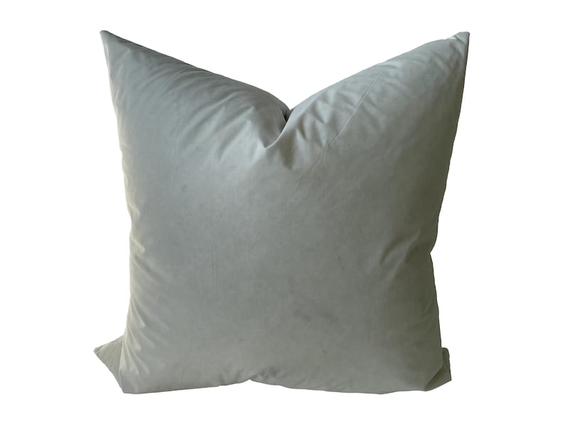 May include: A soft, light grey pillow with a smooth, velvety texture. The pillow is square-shaped and has a simple, understated design.