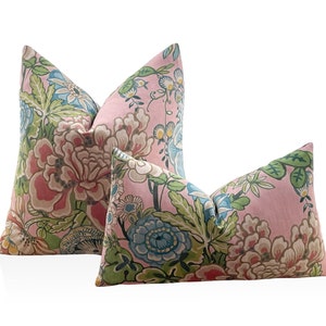 May include: Two pink floral throw pillows with a green and blue floral pattern. The larger pillow is in the background and the smaller pillow is in the foreground.