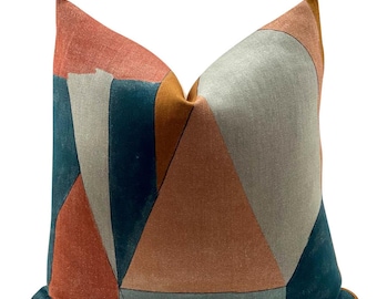 Puede incluir: Una almohada de tiro con estampado geométrico en una combinación de colores turquesa, naranja y rosa. La almohada está hecha de una tela suave y texturizada.