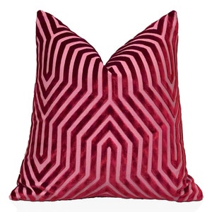 Pode incluir: Uma almofada de veludo rosa com um padrão geométrico. O padrão é composto por linhas sobrepostas que criam uma série de hexágonos.