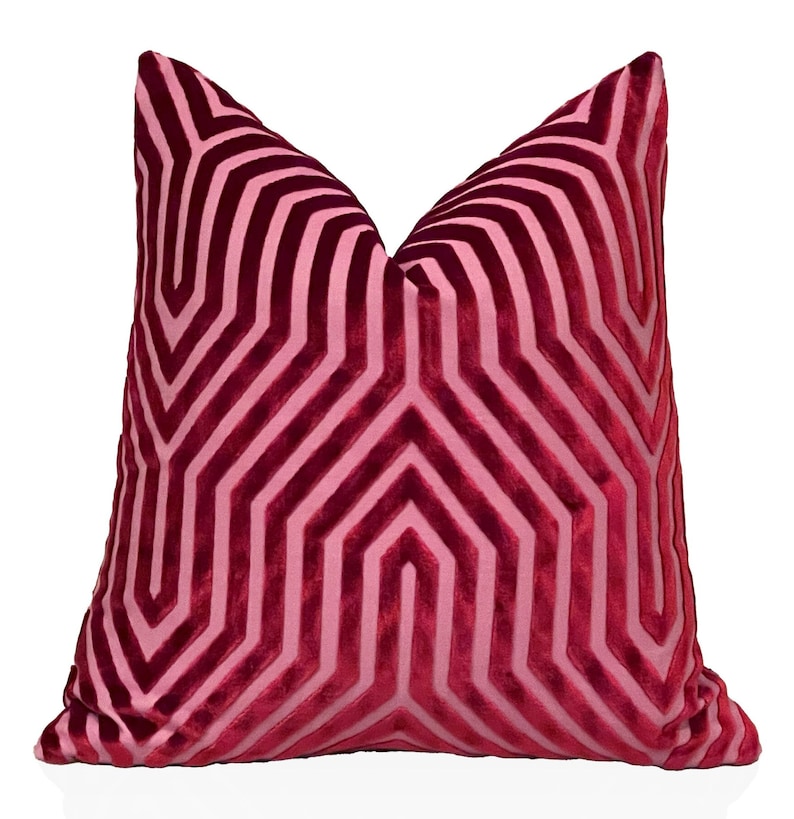 May include: A pink velvet pillow with a geometric pattern. The pattern is made up of overlapping lines that create a series of hexagons.