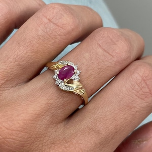 May include: A gold ring featuring a red oval gemstone surrounded by smaller white gemstones.