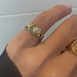 May include: A gold ring with a geometric design featuring a white gemstone and two smaller blue gemstones.