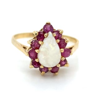 May include: A gold ring featuring a pear-shaped white opal set within a halo of red rubies.