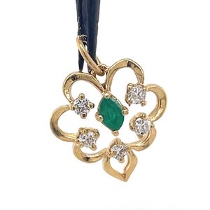 Puede incluir: Un colgante dorado con forma de flor. El colgante presenta una piedra preciosa verde central con talla esmeralda y est&aacute; rodeado de cuatro piedras preciosas claras con talla redonda. El colgante est&aacute; suspendido de un cord&oacute;n negro.