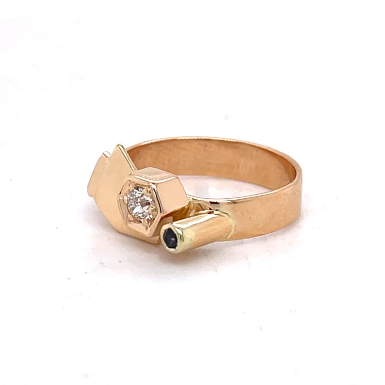 May include: A gold ring with a geometric design featuring a single diamond and a black stone. The ring is made of 14k gold and has a unique, modern style.