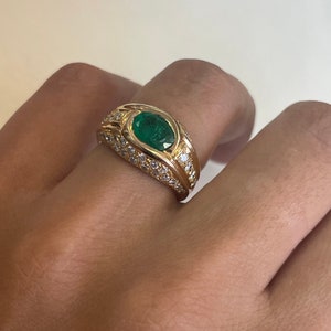 K&ouml;nnte beinhalten: Ein goldener Ring mit einem gro&szlig;en ovalen Smaragd, der von kleineren Diamanten umgeben ist.