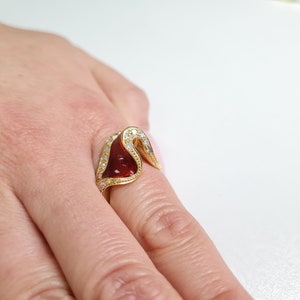 May include: A gold ring with a red stone and clear stones set in the band.
