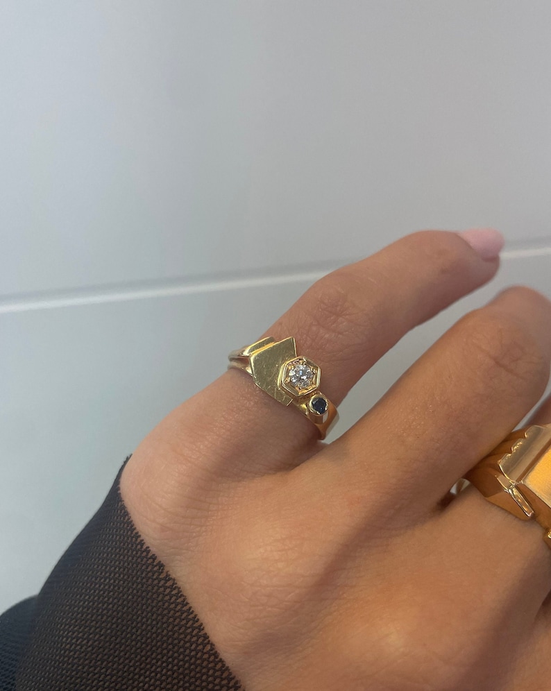 May include: A gold ring with a geometric design featuring a white gemstone and two smaller blue gemstones.