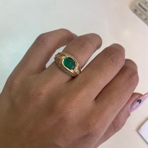 K&ouml;nnte beinhalten: Ein goldener Ring mit einem gro&szlig;en ovalen Smaragd, der von kleineren Diamanten umgeben ist.