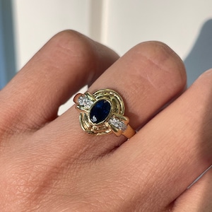 May include: A gold ring with a blue oval gemstone surrounded by smaller clear gemstones.