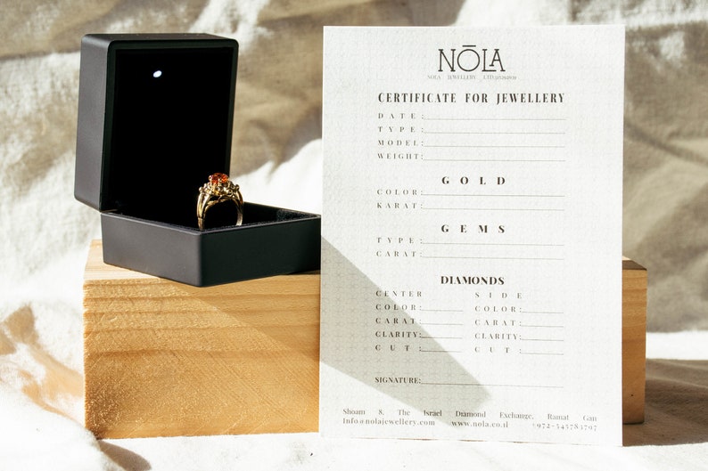 May include: A certificate for jewelry with the text "NOLA" at the top. The certificate has fields for date, type, model, weight, color, karat, gems, type, carat, diamonds, center color, side color, carat, clarity, cut, and signature.