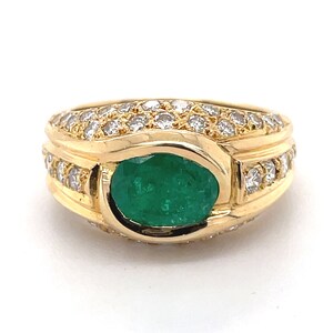 K&ouml;nnte beinhalten: Ein goldener Ring mit einem gro&szlig;en smaragdgr&uuml;nen Edelstein, der von einer Reihe kleiner Diamanten umgeben ist.