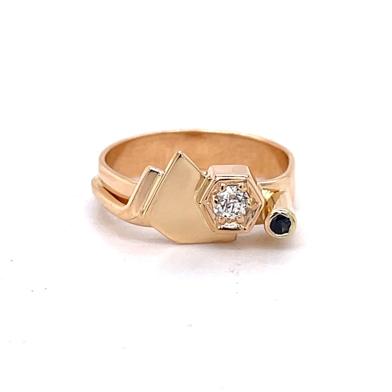 May include: A gold ring with a geometric design featuring a single diamond and a black stone. The ring is made of two bands, one of which is a simple band and the other is a band with a geometric design.