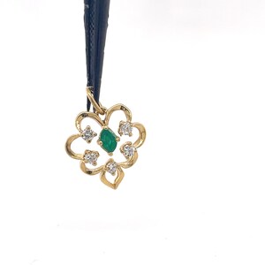 Puede incluir: Colgante de oro con dise&ntilde;o floral, con una gema verde central tallada en esmeralda y cuatro gemas claras circundantes. El colgante est&aacute; suspendido de un cord&oacute;n negro sobre un fondo blanco. El intrincado dise&ntilde;o del colgante a&ntilde;ade elegancia.