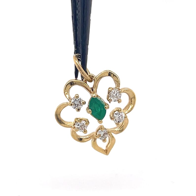 Puede incluir: Un colgante dorado con forma de flor. El colgante presenta una piedra preciosa verde central con talla esmeralda y est&aacute; rodeado de cuatro piedras preciosas claras con talla redonda. El colgante est&aacute; suspendido de un cord&oacute;n negro.