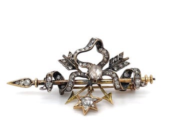 May include: A silver and gold brooch featuring a bow with arrows, a star, and a large diamond-shaped stone.