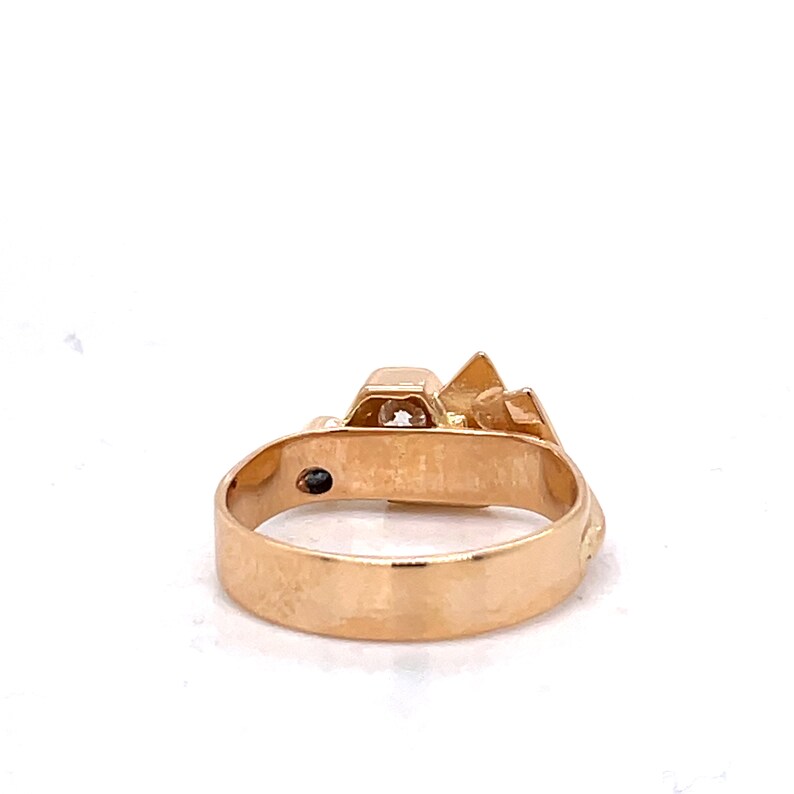 May include: A gold ring with a geometric design featuring a single clear stone in the center.