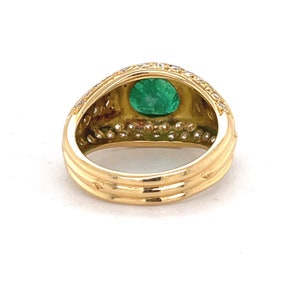 K&ouml;nnte beinhalten: Ein goldener Ring mit einem gro&szlig;en gr&uuml;nen Smaragd, der von kleineren Diamanten umgeben ist. Der Ring hat eine strukturierte Band.