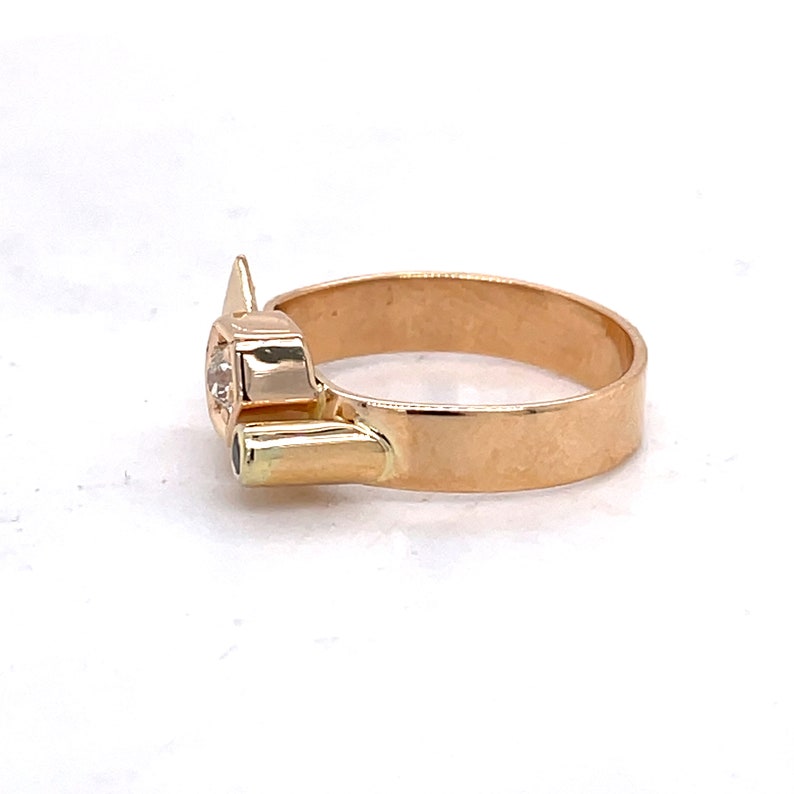 May include: A gold ring with a large, clear gemstone and a smaller, green gemstone. The ring is set in a unique, modern design.