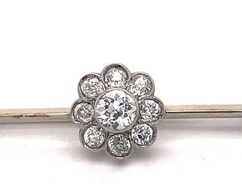 May include: A silver brooch with a central round diamond surrounded by smaller diamonds in a flower shape.