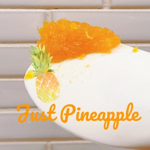 K&ouml;nnte beinhalten: Ein wei&szlig;er L&ouml;ffel mit einem H&auml;ufchen leuchtend orangefarbener Ananasmarmelade. Der L&ouml;ffel ist mit einer Aquarell-Illustration einer Ananas und dem orangefarbenen Schriftzug Just Pineapple auf dem Stiel versehen. Die Fruchtstruktur ist erkennbar.