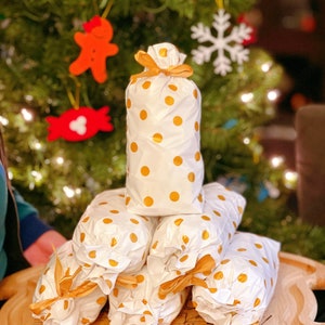 May include: A stack of white gift bags with gold polka dots and gold ribbon bows. The bags are arranged in a pyramid shape on a wooden cutting board. The board has instructions for preparing a turkey.