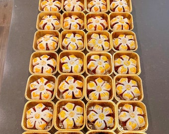 Könnte beinhalten: Nahaufnahme von 36 einzelnen Mondkuchen, die in Reihen in goldfarbenen Behältern angeordnet sind. Jeder Mondkuchen hat eine weiße Teigkruste mit einem blütenförmigen Design und einer roten Füllung.