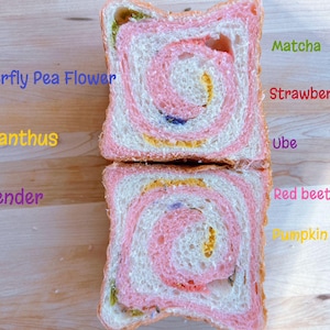May include: Two slices of colorful bread with a swirl pattern, featuring pink, white, yellow, and green hues. The bread is labeled with the words "Matcha", "Strawberry", "Ube", "Red beets", and "Pumpkin". The bread is on a wooden surface.
