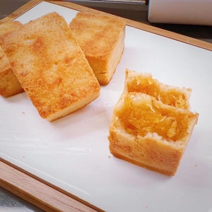 K&ouml;nnte beinhalten: Vier rechteckige Ananaskuchen mit einer goldbraunen, bl&auml;ttrigen Teigkruste. Ein Kuchen ist in der Mitte geteilt und gibt den Blick auf eine durchscheinende, faserige, bernsteinfarbene Ananasmarmeladenf&uuml;llung frei. Die Kuchen liegen auf einem wei&szlig;en Tablett.
