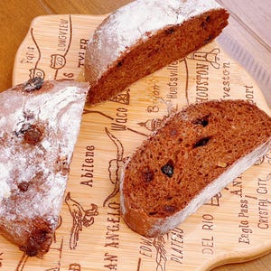 May include: Three slices of chocolate bread with raisins on a wooden cutting board with a map of Texas engraved on it. The bread is dusted with powdered sugar.