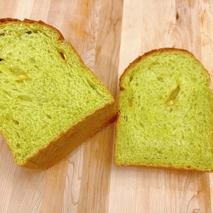 May include: Two slices of green bread on a wooden cutting board. The bread is a light green color and has a soft, fluffy texture.