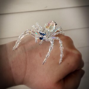 May include: A clear crystal spider with iridescent facets and blue accents. The spider's body is made of multiple clear crystals, with legs and body segments strung together. The spider is a decorative item.