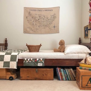 May include: A wooden bed with a green and white checkered quilt, a teddy bear, and a woven basket. The bed is decorated with a map of the United States that says "United States of America".