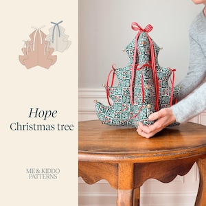 May include: A plush, three-dimensional fabric Christmas tree featuring a green and white botanical print with red berries. The tree is adorned with red ribbon bows at the tips of its branches and small gold-colored bells. Text reads Hope Christmas tree.