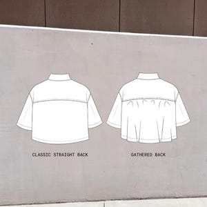 May include: Two white, short-sleeved tops with a high collar are shown against a grey background. One top has a classic straight back, and the other has a gathered back. Text at the bottom reads "CLASSIC STRAIGHT BACK" and "GATHERED BACK."