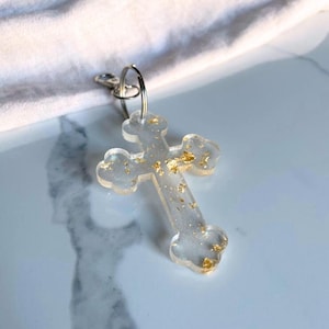 May include: A clear resin cross keychain with gold flecks embedded in the resin. The cross is attached to a silver key ring.