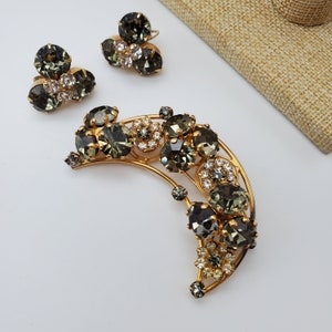 May include: A crescent moon shaped brooch with a gold tone setting and a cluster of dark green and clear rhinestones.