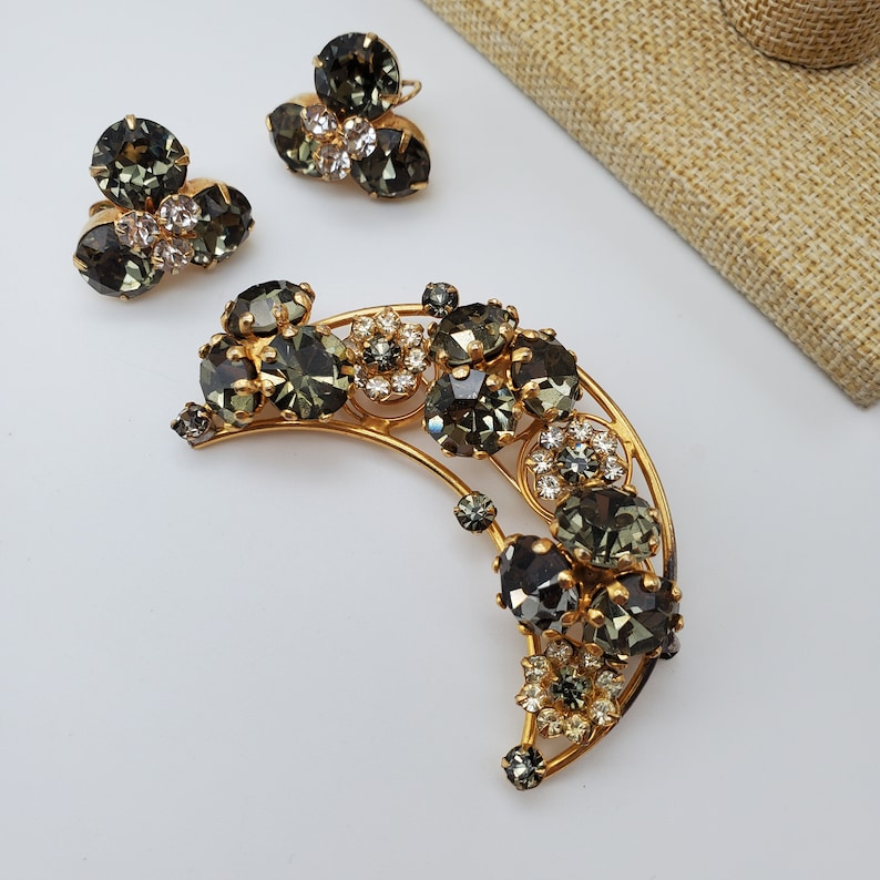 May include: A crescent moon shaped brooch with a gold tone setting and a cluster of dark green and clear rhinestones.