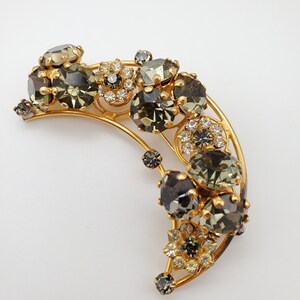 May include: A gold crescent-shaped brooch with a cluster of dark gray and clear rhinestones.
