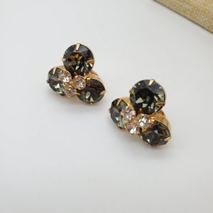 May include: A pair of gold tone earrings with a cluster of three dark green and clear rhinestones.